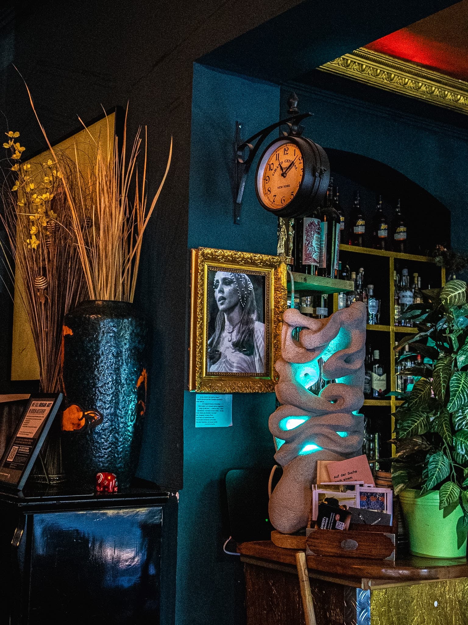 Curated art salon corner at Beetroot Berlin with gilded portrait frame, antique Grand Central station clock, and glowing sculptural lamp